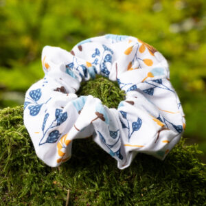 Chouchou personnalisable fait main en tissu à motif floral, posé sur de la mousse verte en forêt.
