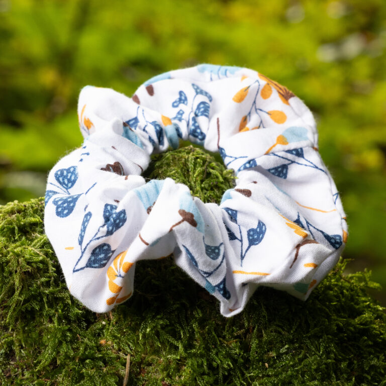 Chouchou personnalisable fait main en tissu à motif floral, posé sur de la mousse verte en forêt.