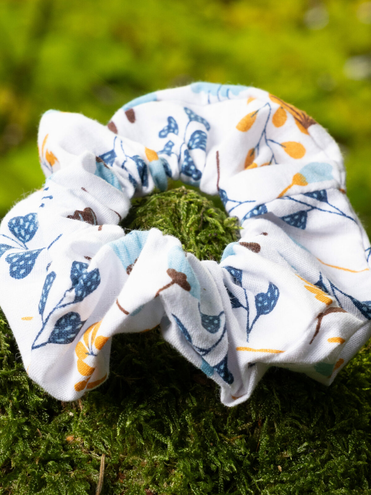 Chouchou personnalisable fait main en tissu à motif floral, posé sur de la mousse verte en forêt.